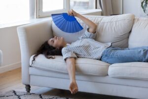 Homeowner lying on couch fanning themselves with hand fan