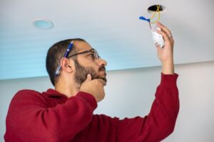 Homeowner looking confused and inspecting electrical wires of smoke detector