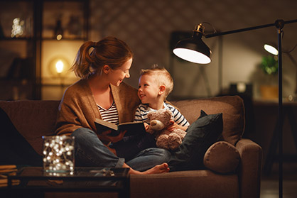Mother and son sitting on a couch reading a book under a lamp