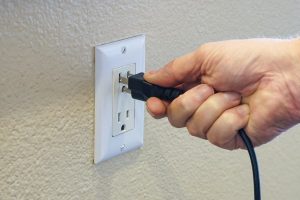 Homeowner plugging electronic device into wall outlet while using electrical generator 